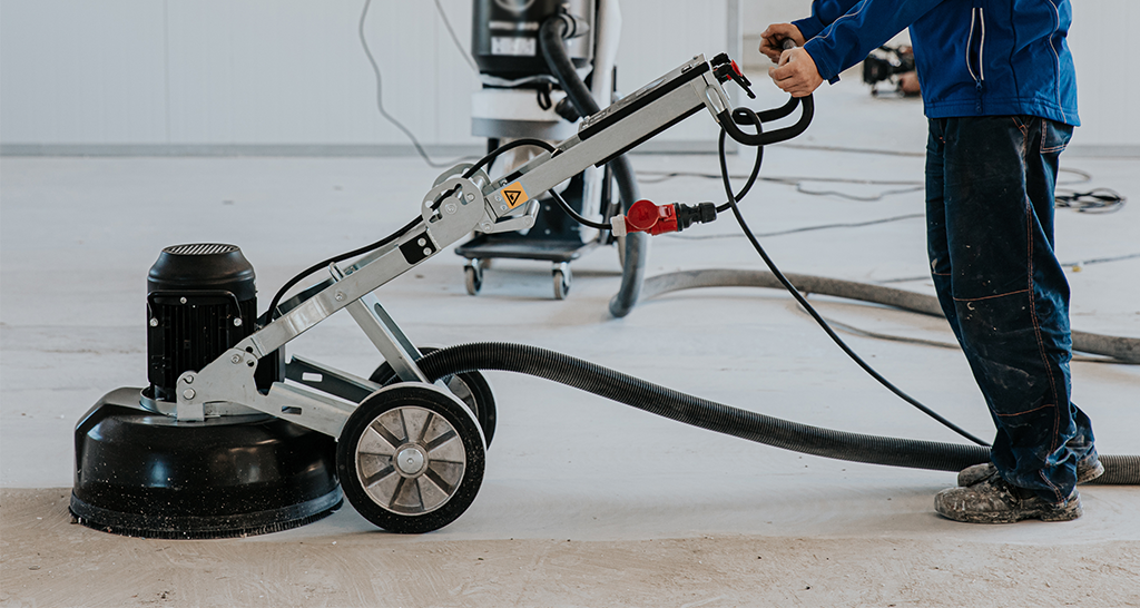 Ouvrier utilisant une machine de ponçage pour préparer un sol industriel